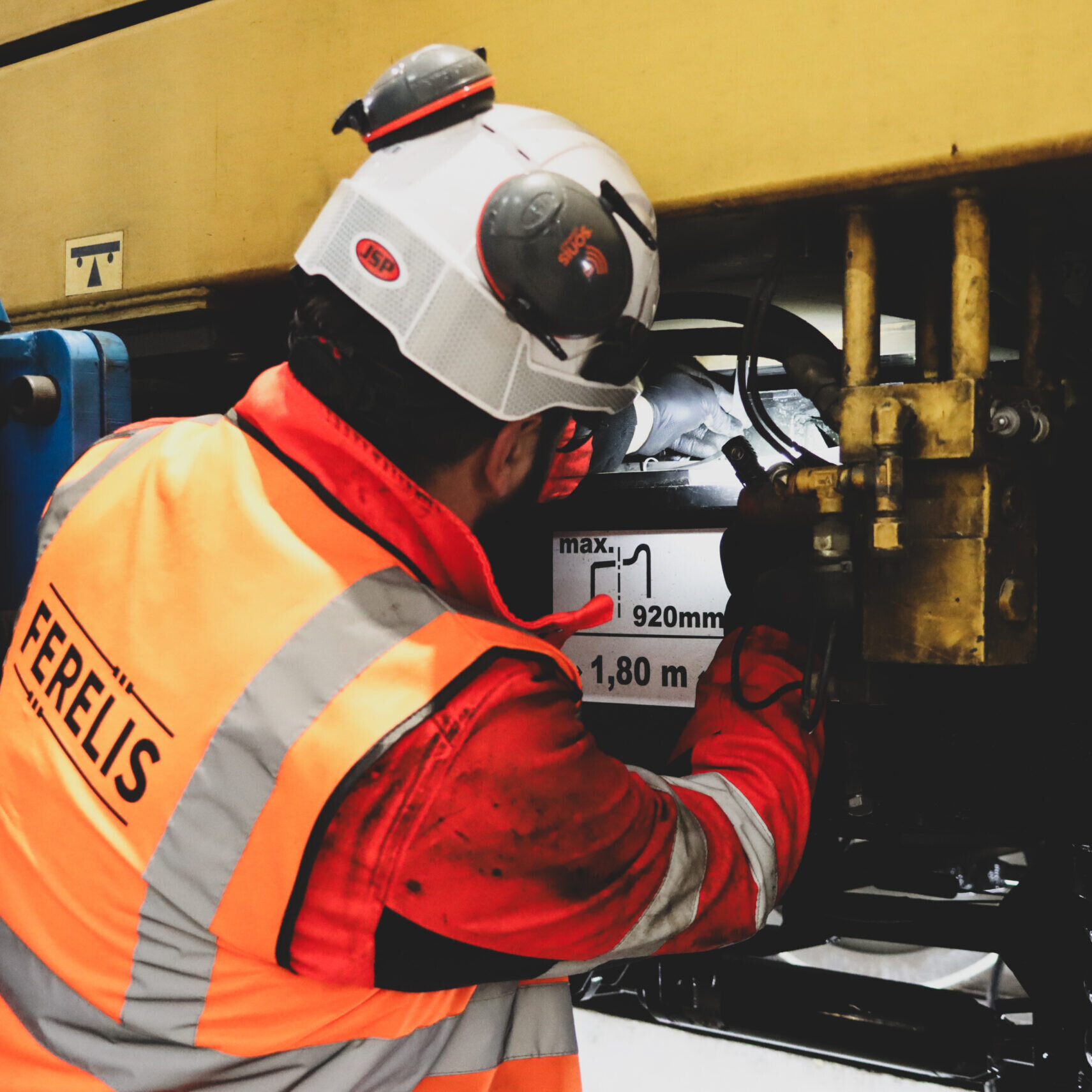 Technicien FERELIS équipé de protections individuelles réalisant une opération de maintenance sur un engin ferroviaire en atelier.