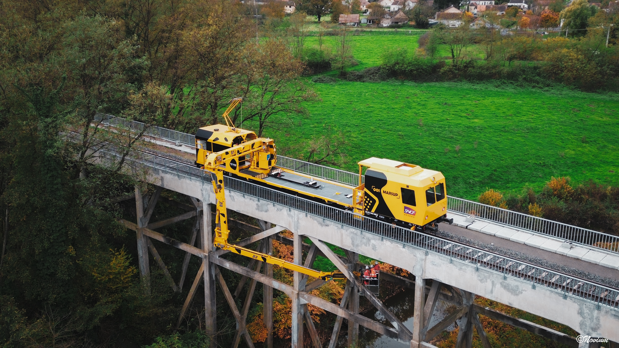 Engin ferroviaire MARSUP de NOVIUM sur un pont, avec son bras articul&eacute; et sa nacelle d&eacute;ploy&eacute;s sous l'ouvrage.
